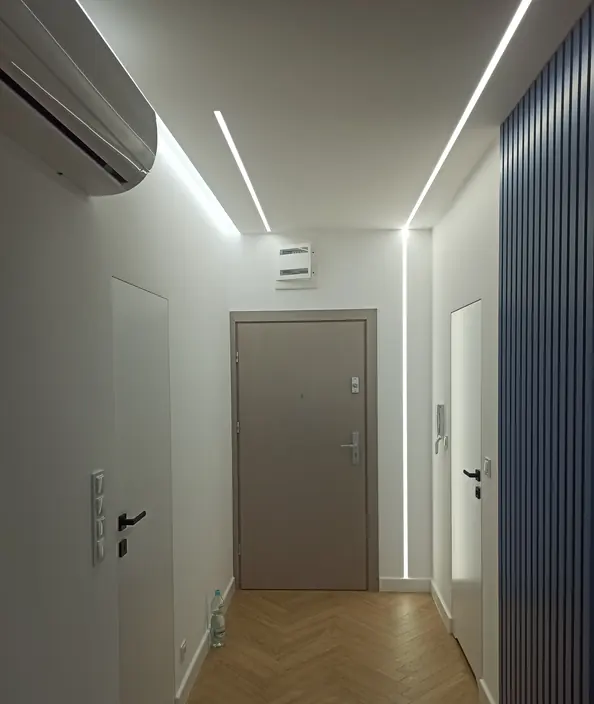 Korytarz z ryflowaną ścianą, liniowym oświetleniem LED i jasnymi drzwiami