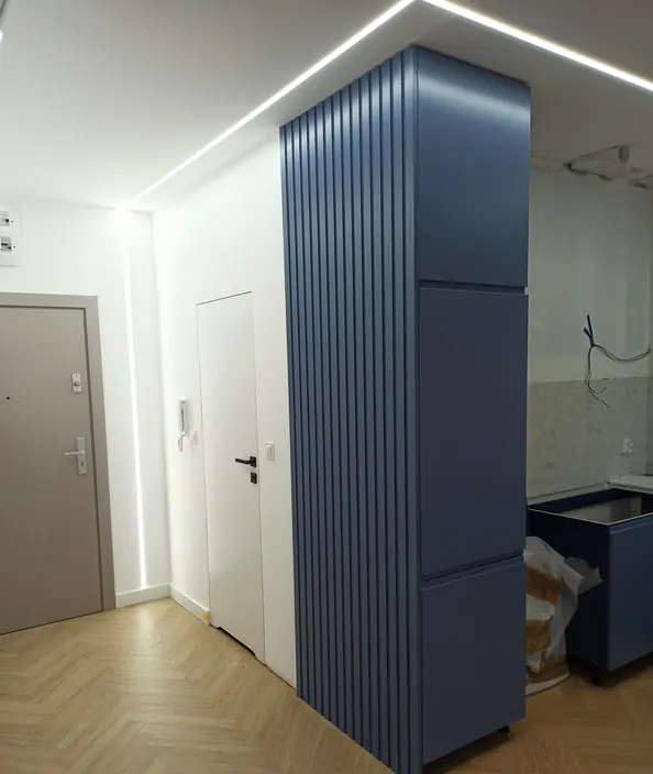 Przedpokój z niebieską ryflowaną zabudową i podłogą w jodełkę