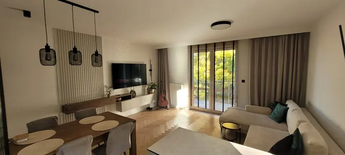 Salon połączony z jadalnią, lampy wiszące nad stołem, wyjście na ogród