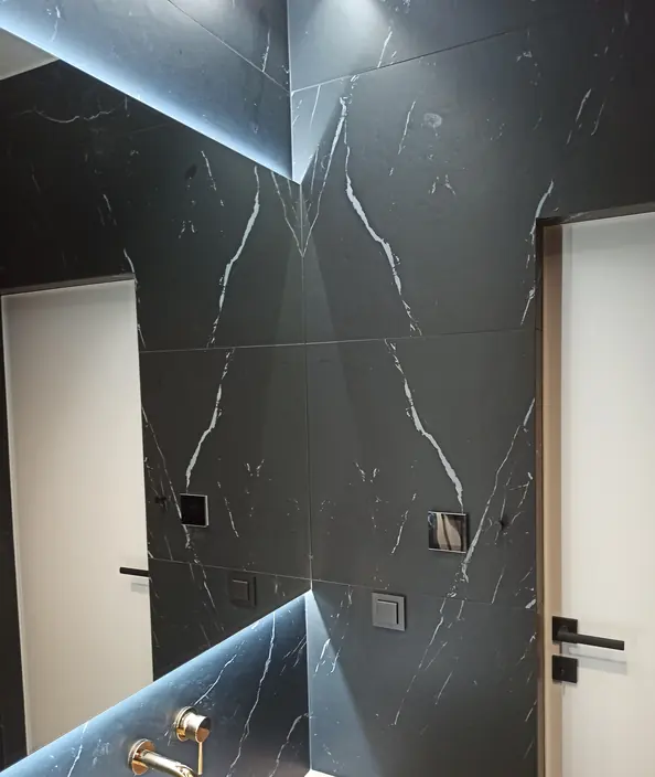 Toaleta z czarnym marmurem na ścianie i złotą baterią nad umywalką
